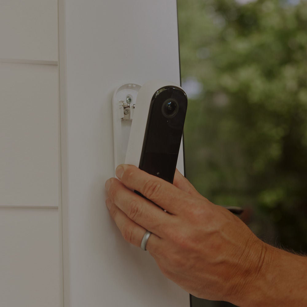 a hand attaches a video doorbell to a front door