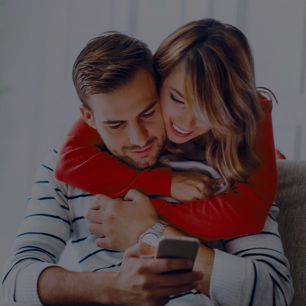  Ein Paar umarmt sich und schaut dabei auf den Bildschirm eines Mobiltelefons