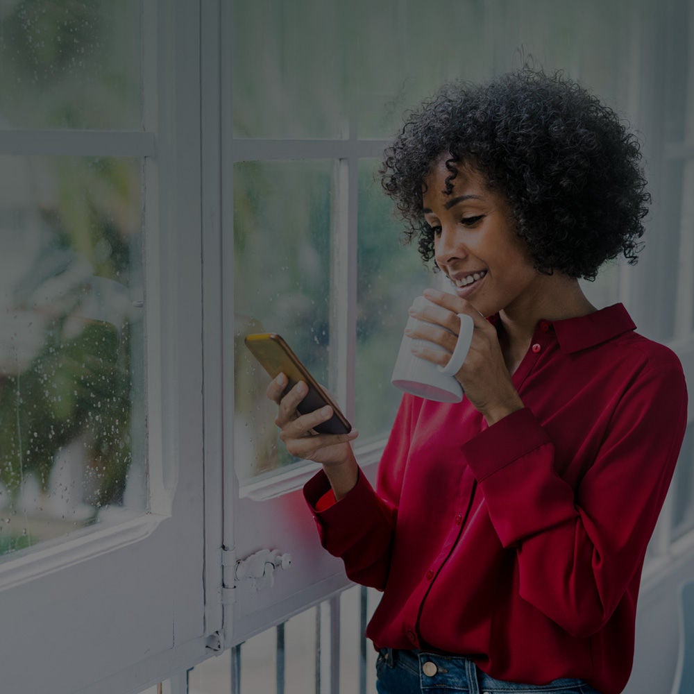 a woman drinks her coffee whilst happily looking at her mobile phone